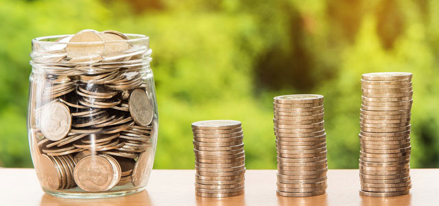 A photo of 3 stacks of quarters and a glass jar full of change.